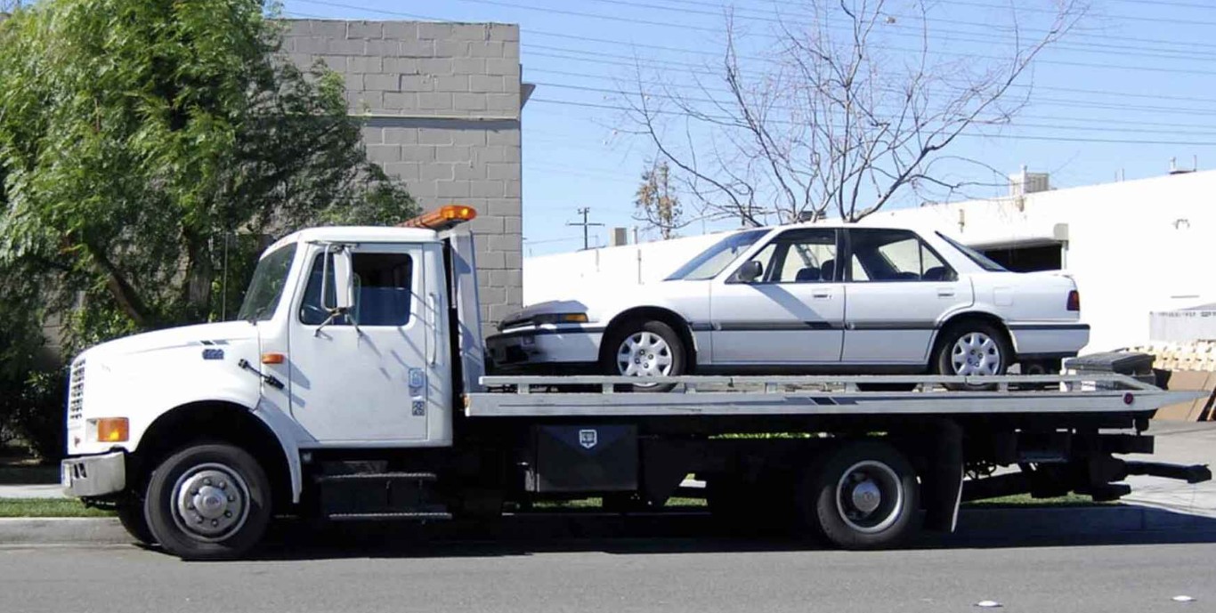 Flatbed towing service transporting white sedan safely in Norwalk, CT